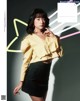 A woman in a yellow blouse and black skirt posing for a magazine.